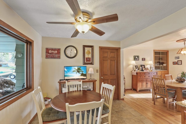 dining area with ceiling fan with notable chandelier, a textured ceiling, and light wood-type flooring