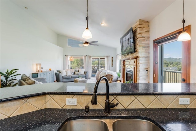 kitchen featuring vaulted ceiling, a stone fireplace, pendant lighting, sink, and ceiling fan