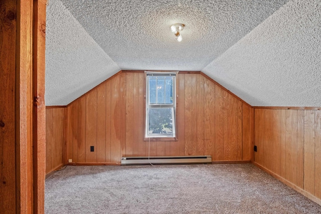 additional living space with vaulted ceiling, a baseboard heating unit, light colored carpet, and wood walls