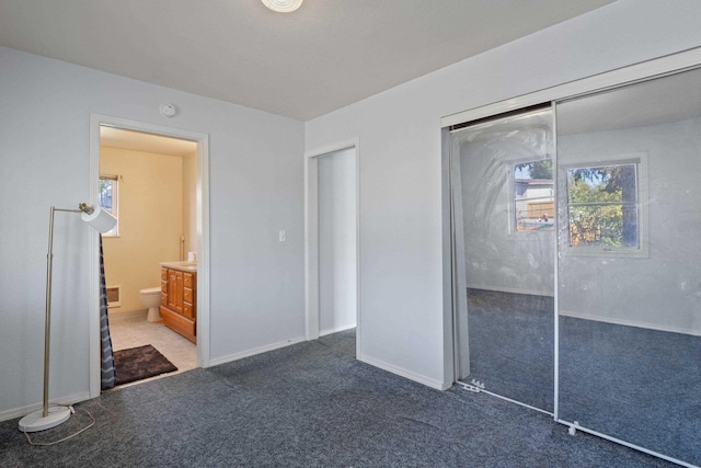 unfurnished bedroom with ensuite bathroom, a closet, and dark colored carpet