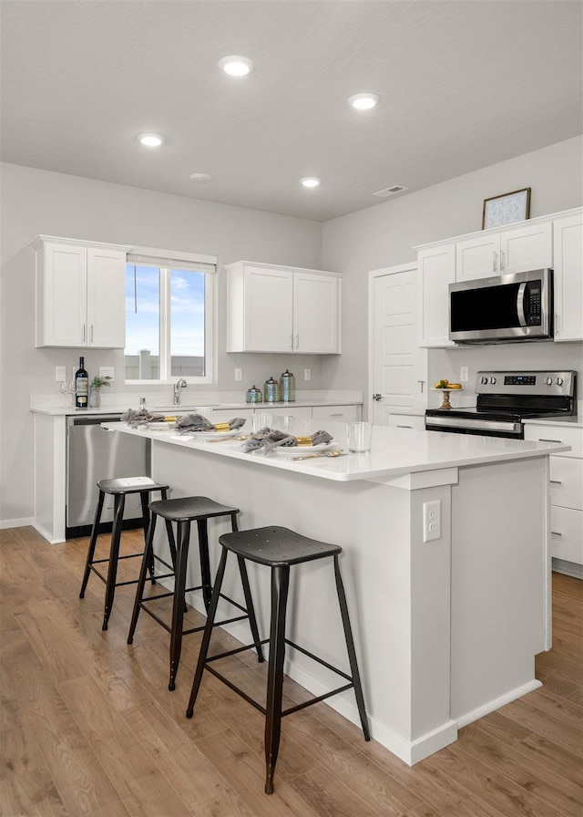 kitchen with appliances with stainless steel finishes, a kitchen bar, a kitchen island, and white cabinets