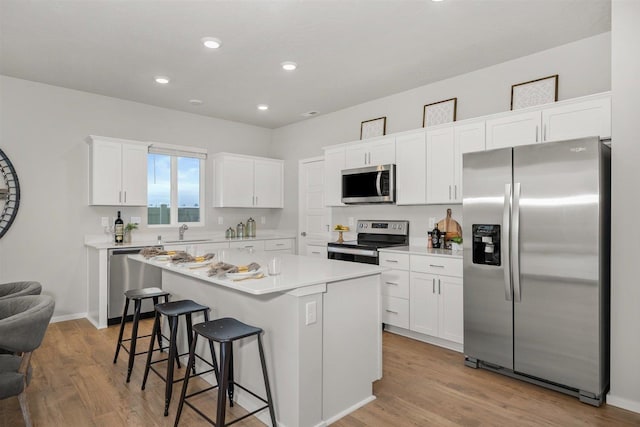 kitchen with a kitchen island, white cabinets, a kitchen bar, light hardwood / wood-style floors, and stainless steel appliances