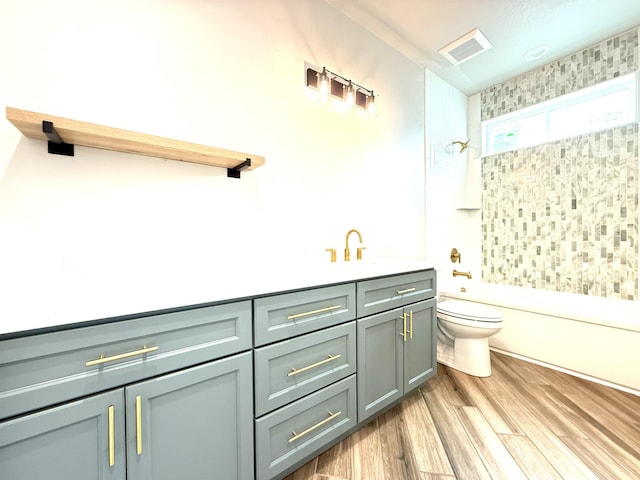 full bath featuring wood finished floors, visible vents, toilet, shower / washtub combination, and vanity