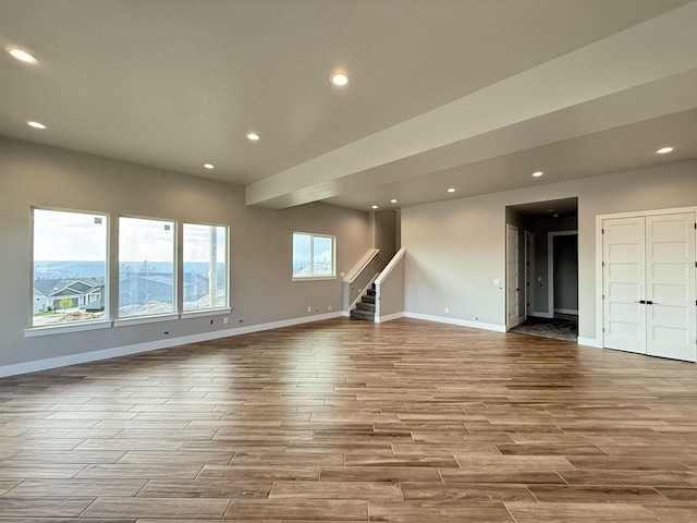 unfurnished living room featuring baseboards, recessed lighting, wood finished floors, and stairs