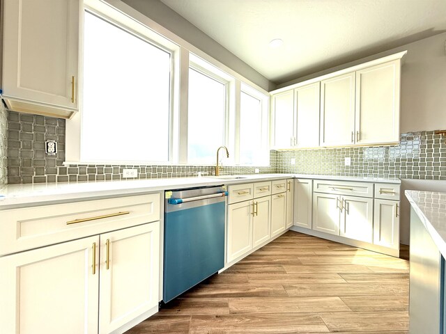 kitchen featuring stainless steel dishwasher, a sink, light countertops, light wood finished floors, and backsplash