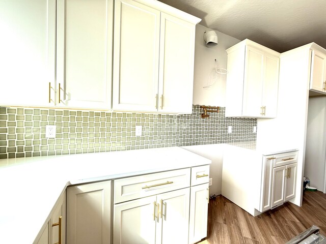 kitchen with tasteful backsplash, white cabinetry, wood finished floors, and light countertops