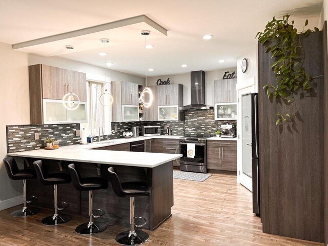 kitchen featuring appliances with stainless steel finishes, wall chimney range hood, a kitchen bar, and kitchen peninsula