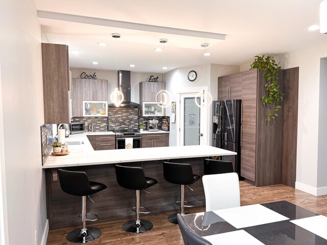 kitchen with decorative light fixtures, stainless steel range with electric stovetop, kitchen peninsula, black fridge, and wall chimney exhaust hood