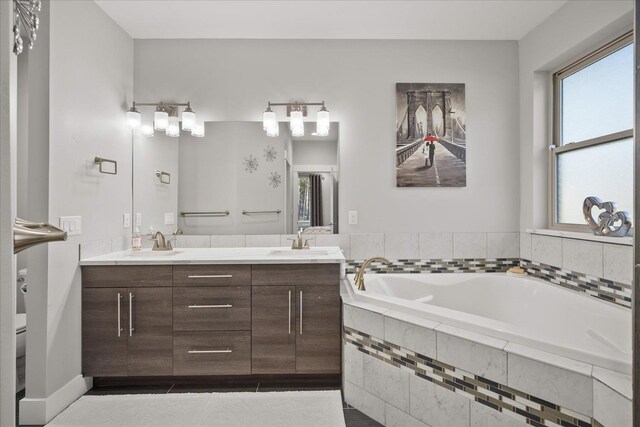 bathroom with a relaxing tiled tub, vanity, and tile patterned flooring