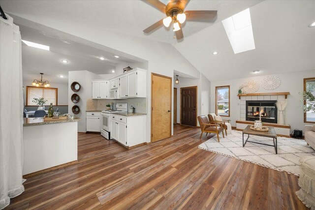 kitchen featuring white appliances, lofted ceiling with skylight, light stone countertops, white cabinets, and a tiled fireplace