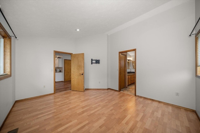 unfurnished bedroom featuring lofted ceiling, ensuite bath, light hardwood / wood-style floors, and a textured ceiling