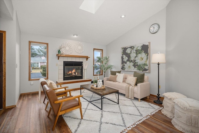 living room featuring wood-type flooring, a tile fireplace, and vaulted ceiling with skylight