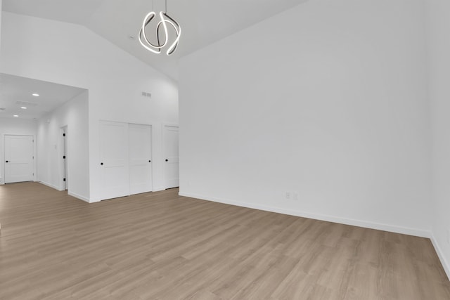 spare room featuring high vaulted ceiling, a notable chandelier, and light hardwood / wood-style floors