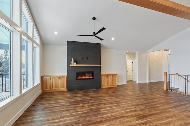 unfurnished living room featuring dark hardwood / wood-style flooring, high vaulted ceiling, a tile fireplace, and ceiling fan