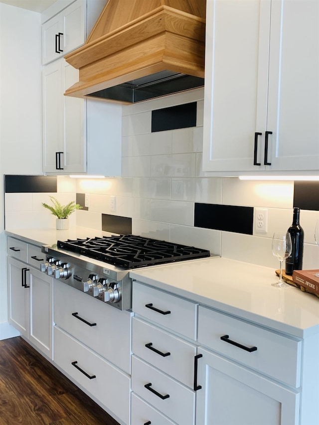 kitchen featuring premium range hood, stainless steel gas stovetop, white cabinetry, backsplash, and dark wood-type flooring