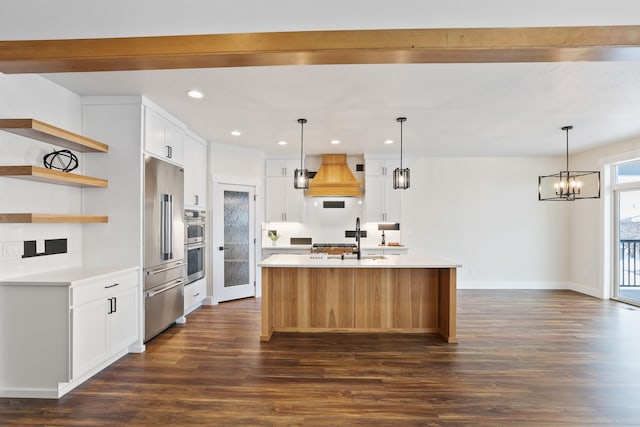 kitchen with stainless steel appliances, a kitchen island with sink, custom range hood, and white cabinets