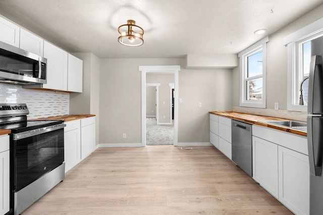 kitchen featuring butcher block countertops, white cabinetry, decorative backsplash, light hardwood / wood-style floors, and stainless steel appliances