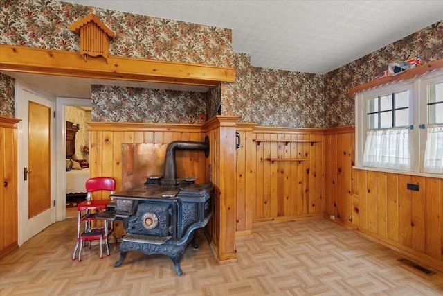 interior space with a textured ceiling, wooden walls, light parquet floors, and a wood stove