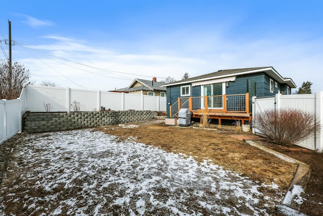 snow covered rear of property with a deck and a fenced backyard