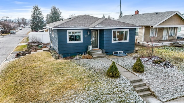 bungalow with fence, a front yard, and a shingled roof