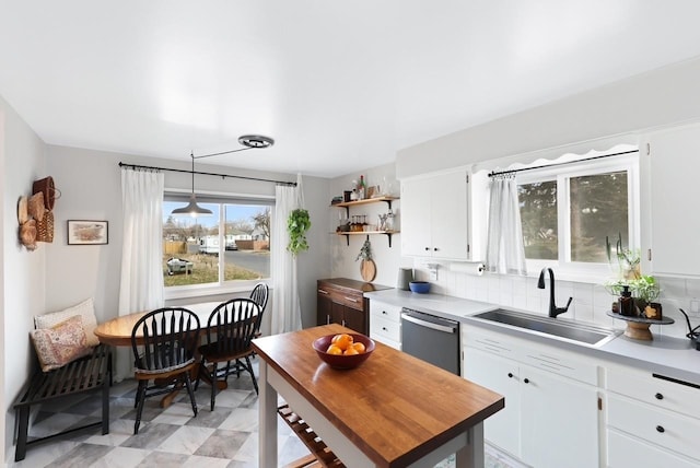 kitchen featuring tasteful backsplash, white cabinetry, sink, hanging light fixtures, and stainless steel dishwasher