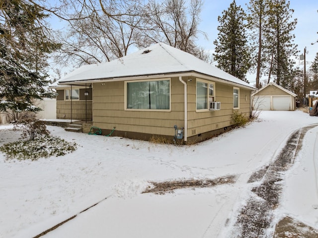 view of snowy exterior featuring cooling unit, a garage, and an outbuilding