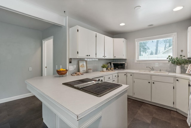 kitchen with tasteful backsplash, white cabinetry, sink, and kitchen peninsula