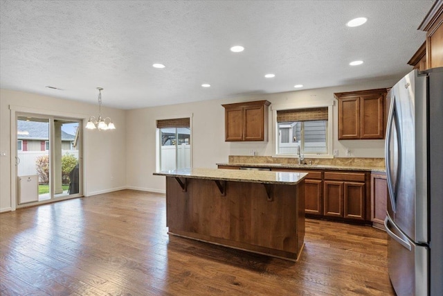 kitchen with pendant lighting, dark wood-type flooring, stainless steel refrigerator, a kitchen island, and a kitchen bar