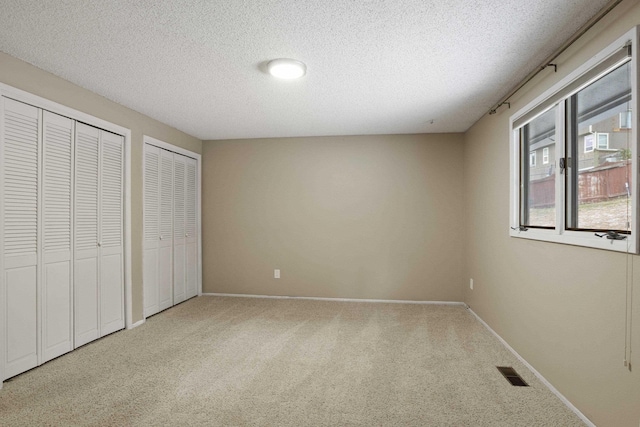 unfurnished bedroom with multiple closets, carpet floors, and a textured ceiling