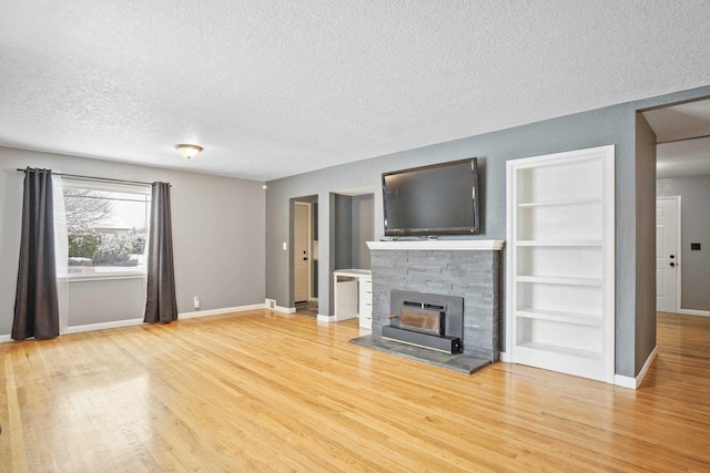 unfurnished living room featuring built in shelves, a fireplace, light hardwood / wood-style floors, and a textured ceiling