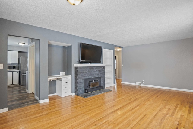 unfurnished living room with a stone fireplace, a textured ceiling, and light wood-type flooring