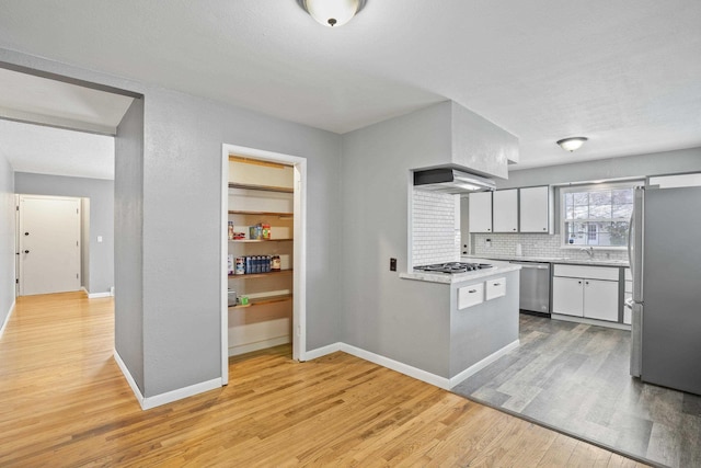 kitchen featuring sink, appliances with stainless steel finishes, light hardwood / wood-style floors, decorative backsplash, and wall chimney exhaust hood