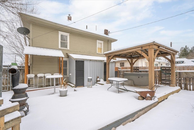 snow covered back of property featuring a gazebo and a hot tub