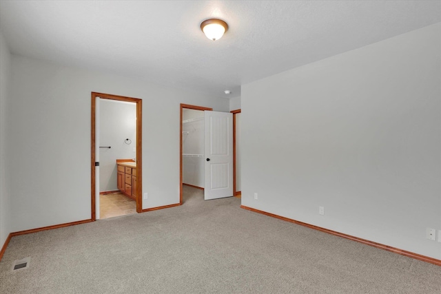 unfurnished bedroom with connected bathroom, a spacious closet, light carpet, a textured ceiling, and a closet