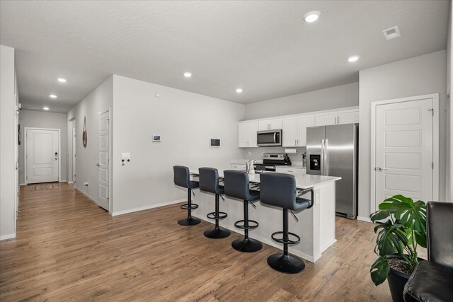 kitchen featuring white cabinets, light countertops, appliances with stainless steel finishes, light wood finished floors, and a kitchen bar