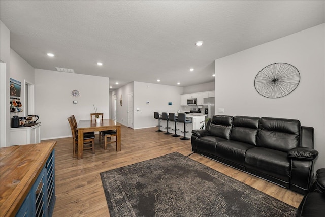 living room featuring recessed lighting, visible vents, a textured ceiling, light wood-type flooring, and baseboards