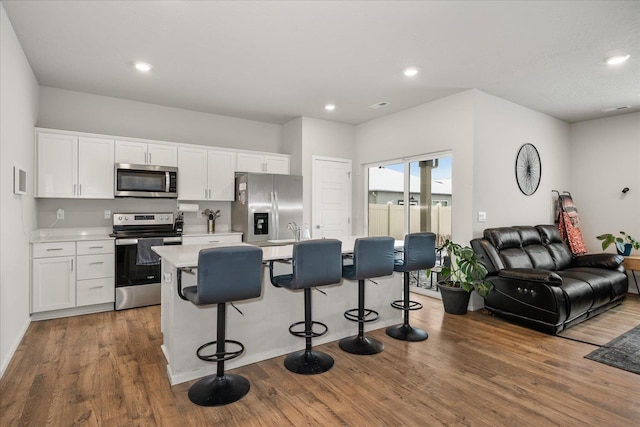 kitchen featuring wood finished floors, open floor plan, light countertops, appliances with stainless steel finishes, and a center island with sink