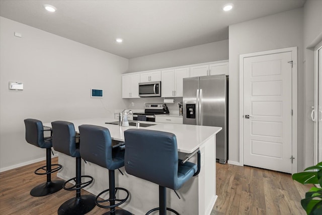 kitchen with stainless steel appliances, dark wood-type flooring, white cabinetry, a kitchen breakfast bar, and light countertops