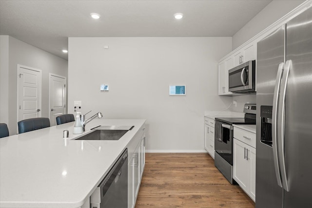 kitchen featuring wood finished floors, a sink, white cabinets, appliances with stainless steel finishes, and a center island with sink