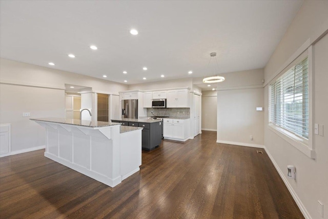 kitchen with appliances with stainless steel finishes, light stone counters, white cabinets, a center island with sink, and decorative light fixtures