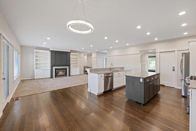 kitchen with white cabinetry, a large fireplace, hanging light fixtures, stainless steel appliances, and light stone countertops