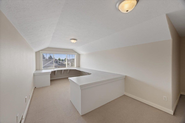 unfurnished office featuring lofted ceiling, built in desk, light carpet, and a textured ceiling