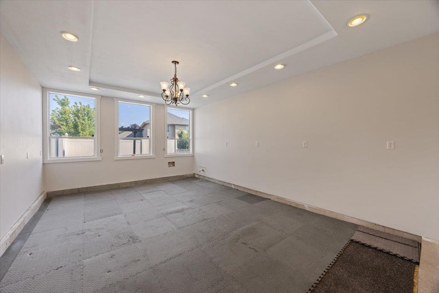 empty room featuring light carpet, a tray ceiling, and a chandelier