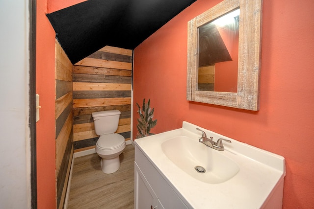 bathroom with vanity, wood-type flooring, toilet, and wood walls