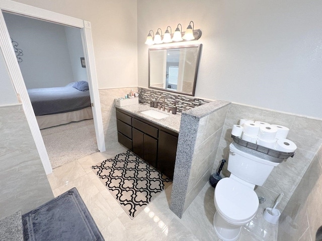 bathroom featuring vanity, connected bathroom, toilet, wainscoting, and tile walls