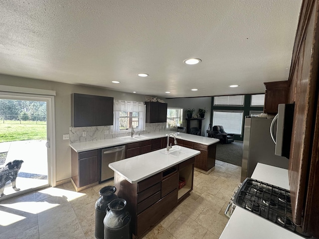 kitchen with stainless steel dishwasher, an island with sink, tasteful backsplash, a sink, and light countertops