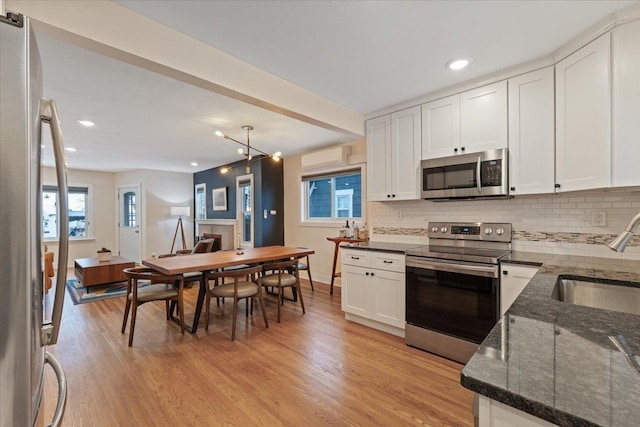 kitchen featuring appliances with stainless steel finishes, decorative light fixtures, white cabinetry, sink, and light hardwood / wood-style floors