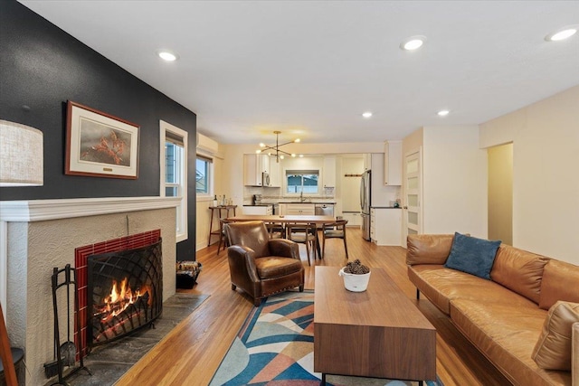 living room with a chandelier, sink, a tiled fireplace, and hardwood / wood-style floors