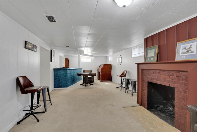 basement featuring light carpet, a brick fireplace, and visible vents