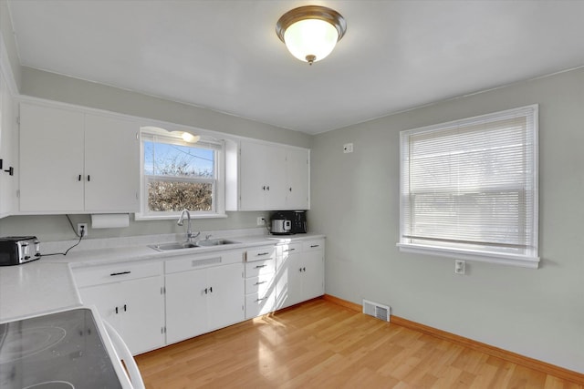 kitchen featuring visible vents, white cabinets, light countertops, light wood-style floors, and a sink